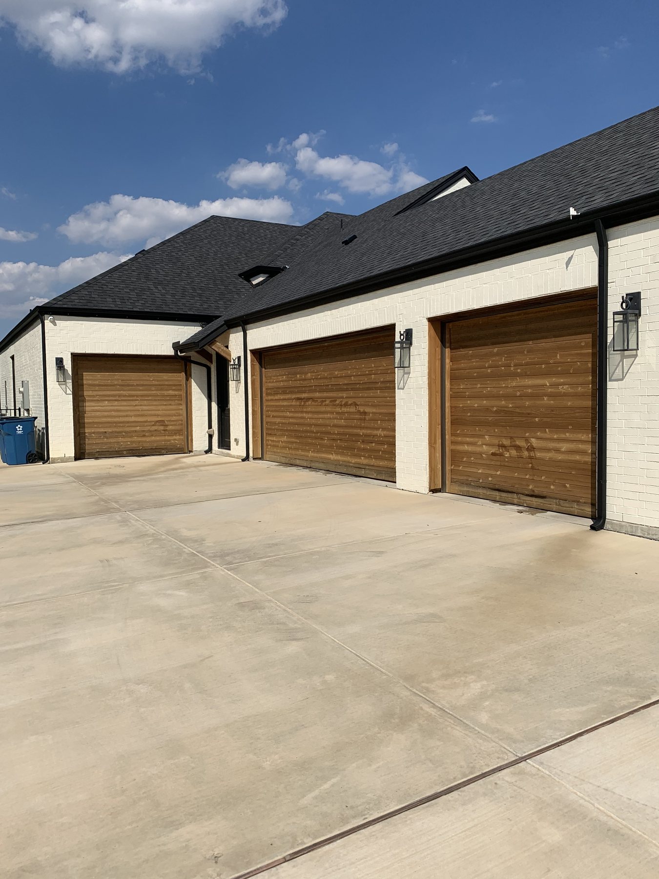 A white brick Dallas estate with natural wood garage doors finished by Prime Estate Services